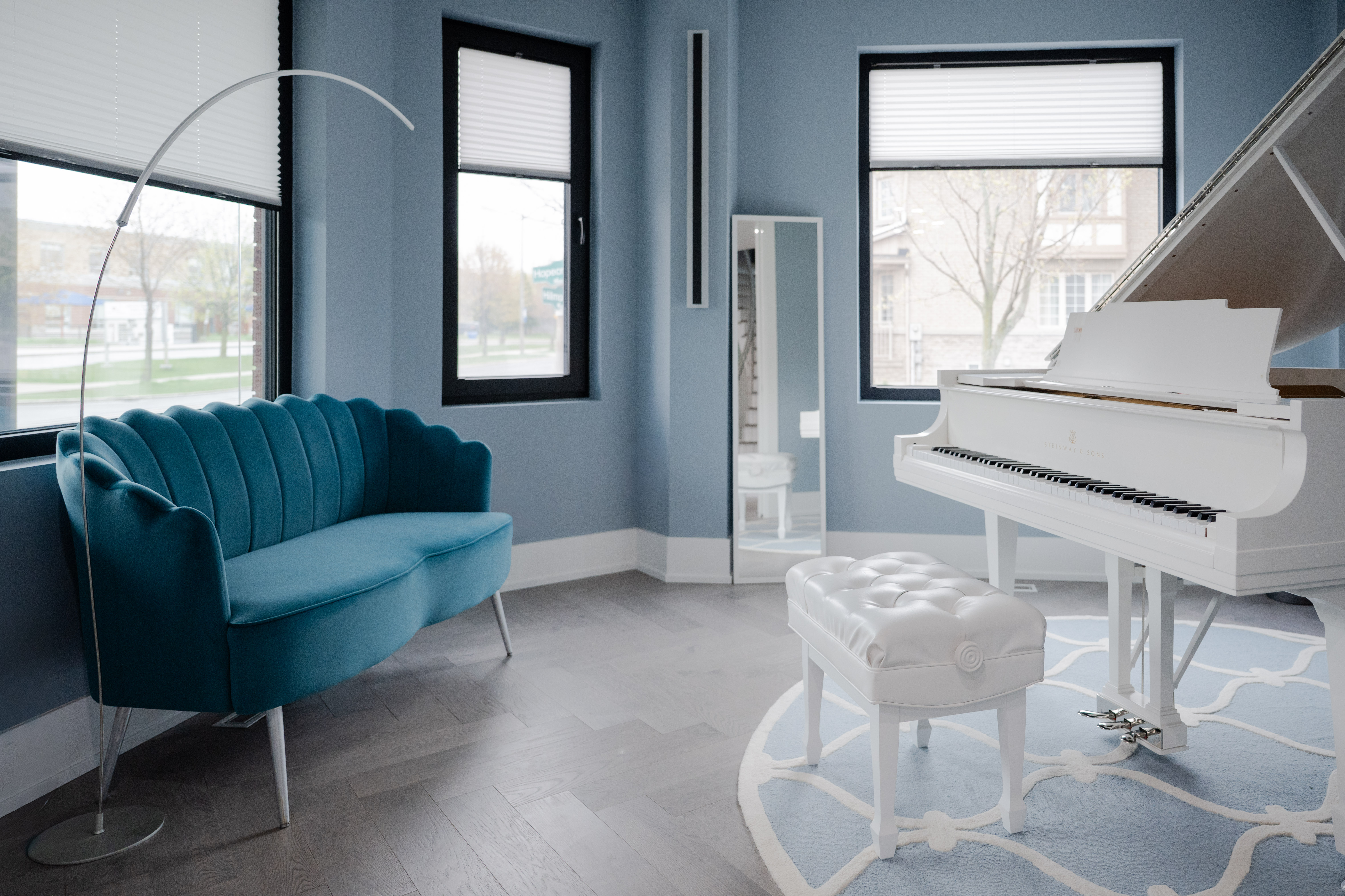 White grand piano, bench, rug, windows, and guitars in the studio